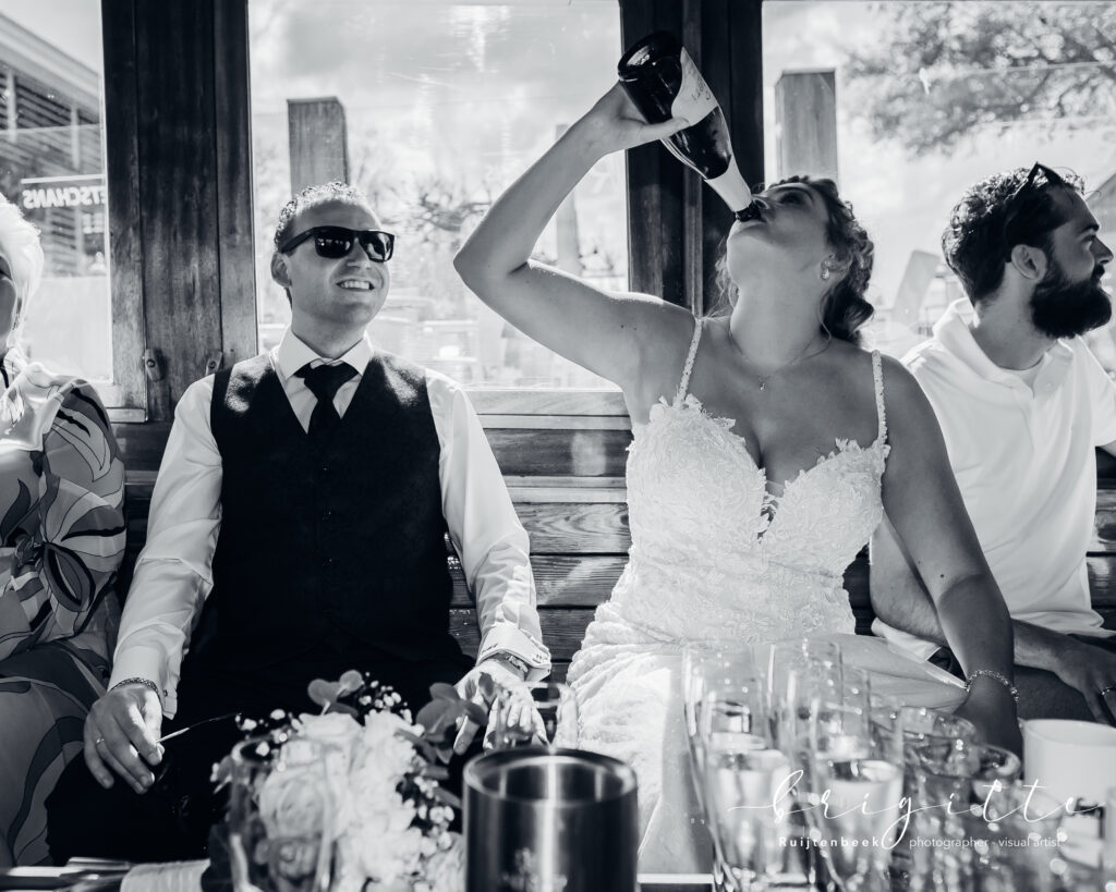 Aan boord van rondvaartboot, bruid drinkt uit champagnefles en bruidegom zit met zonnebril op te kijken