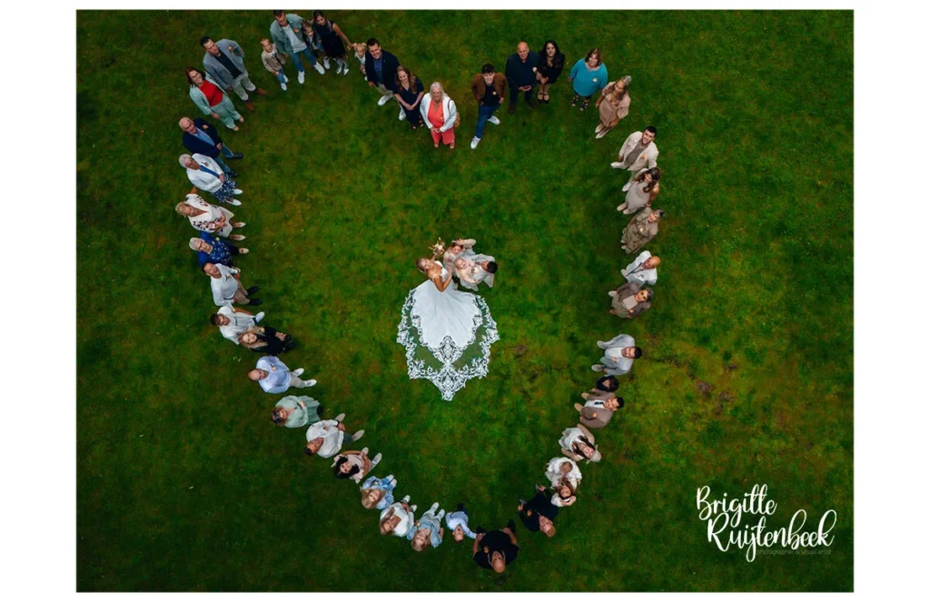 Dronefoto van bruidspaar met familie en vrienden in hartvorm op het grasveld bij Slotplaats Bakkeveen