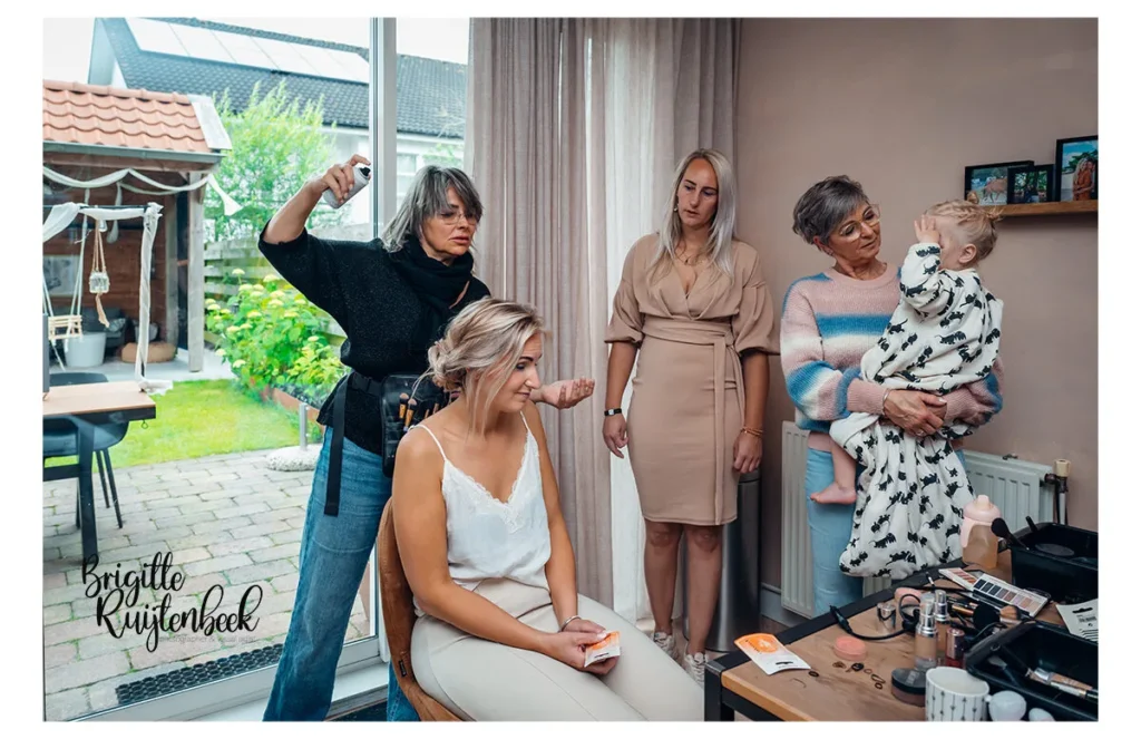 Bruid wordt gestyled in huis terwijl moeder, zus en dochter toekijken tijdens de voorbereiding op haar trouwdag.