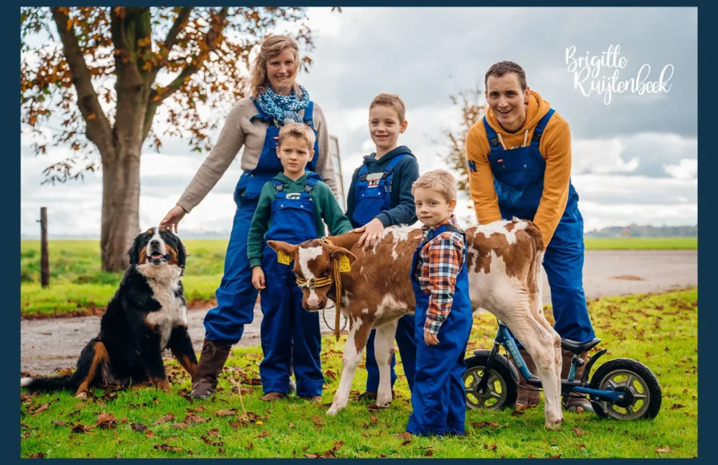 Gezin in blauwe overalls poseert met een kalf en hun hond op een boerderij in Groningen tijdens een Day in the Life fotoshoot.