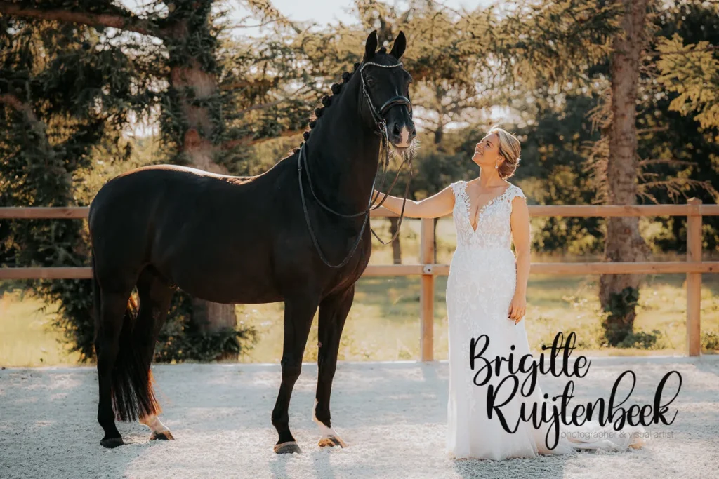 Bruidsfoto van Wytske in haar trouwjurk met haar zwarte paard Igor in de paddock bij hun boerderij in Kolham.