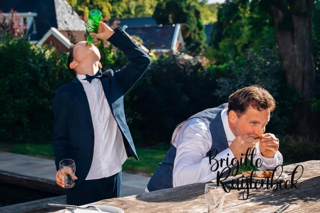 Bruidegom en zoon genieten van het diner; zoon neemt stiekem een slokje bier tijdens bruiloft op boerderij in Kolham.

