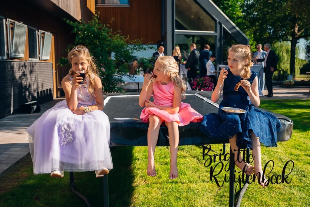 Drie meisjes in feestjurken eten en drinken op een trampoline tijdens trouwfeest in Kolham.