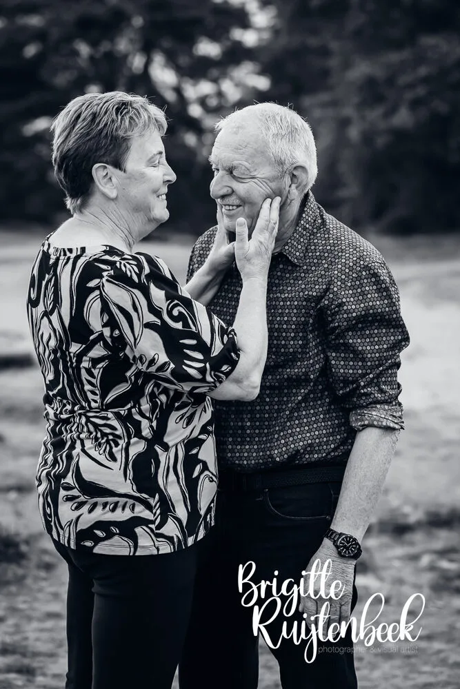 Opa en oma kijken elkaar liefdevol aan tijdens een familiefotoshoot in zwart-wit