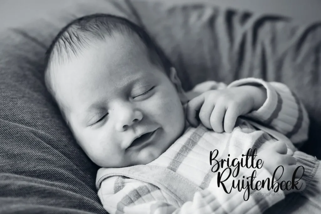 Close-up zwart-wit portret van een lachende baby tijdens een newbornshoot aan huis.