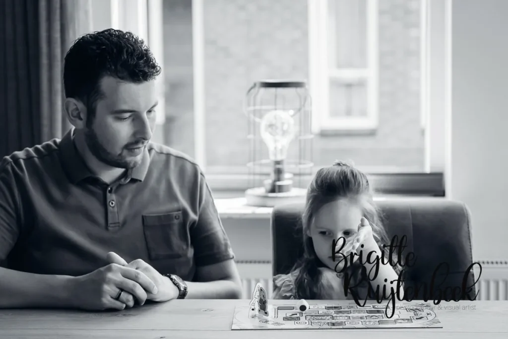 Vader en dochter spelen samen een gezelschapsspel aan tafel tijdens de newbornshoot.