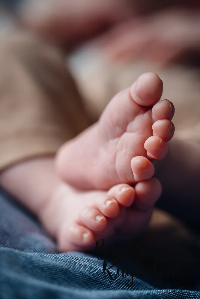 Close-up van babyvoetjes in natuurlijk licht tijdens een newbornshoot thuis.
