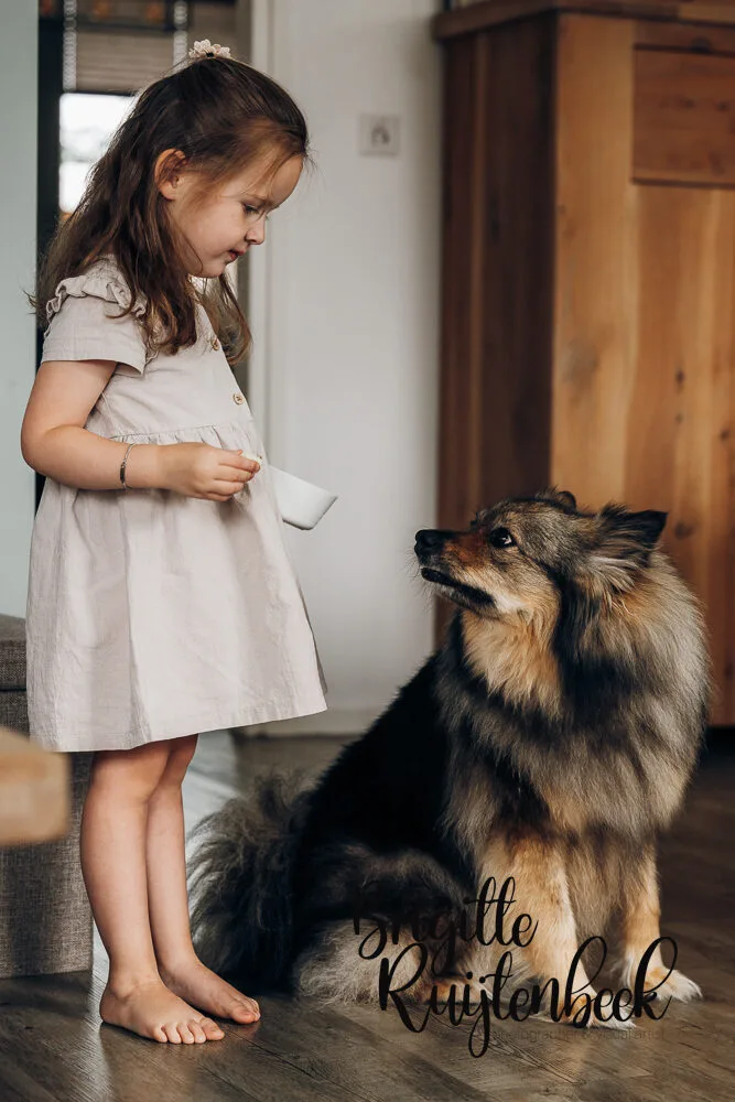 Grote zus deelt een speels moment met de hond in de woonkamer tijdens een newbornshoot.