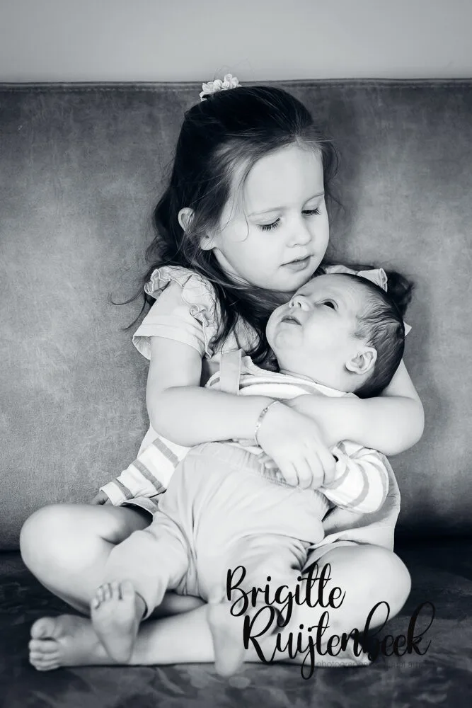 Zwart-wit portret van een meisje dat haar babybroertje op schoot heeft.