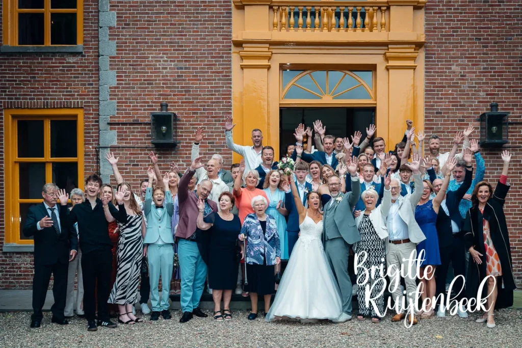 Groepsfoto van het bruidspaar en hun gasten voor de ingang van de Fraeylemaborg.