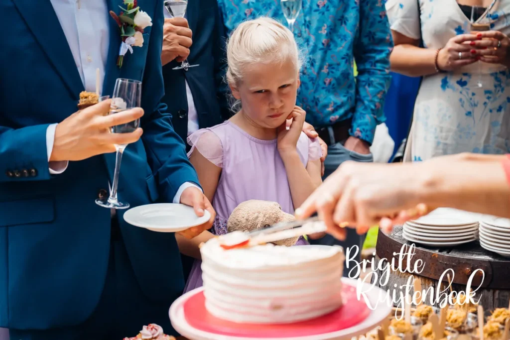 Jong meisje in lila jurk kijkt nieuwsgierig naar de bruidstaart tijdens het huwelijksfeest.