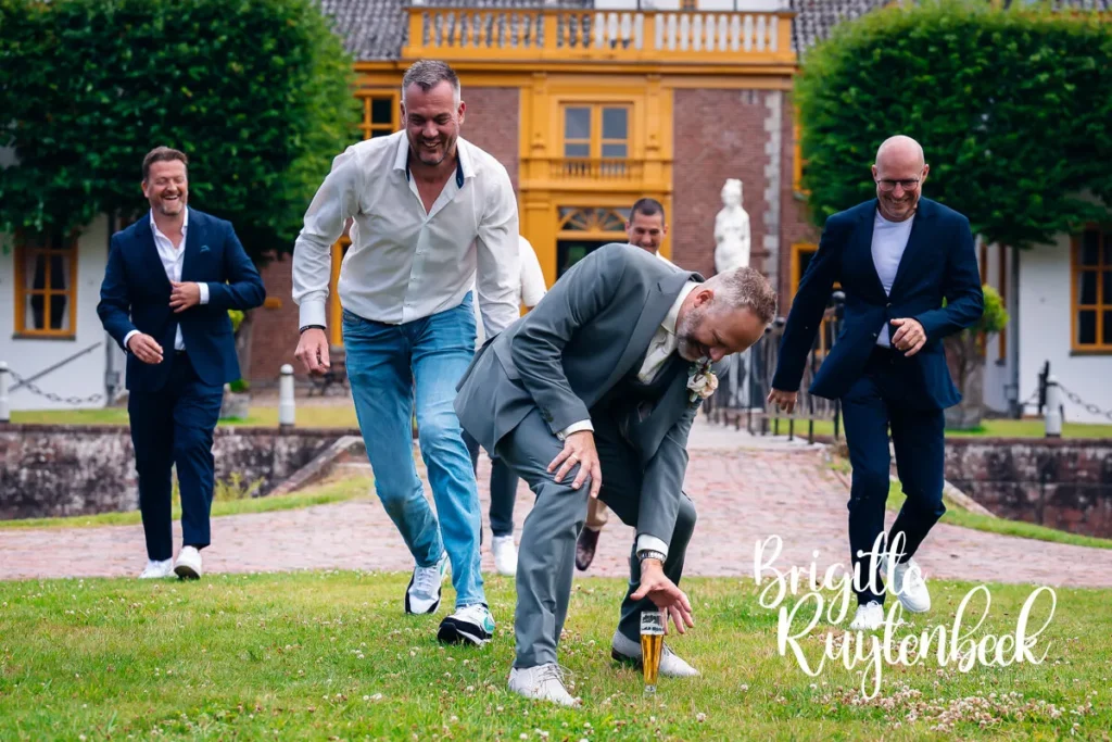 Bruidegom rent lachend met vrienden over het gras om een glas bier te pakken bij Restaurant de Boerderij naast de Fraeylemaborg in Slochteren.