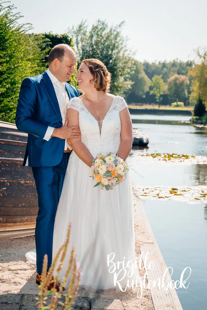 Bruidspaar Sandra en David lachend tijdens fotoshoot aan het water op hun trouwdag, voorafgaand aan de ceremonie bij Trouwboerderij Mausel in Noordbroek.