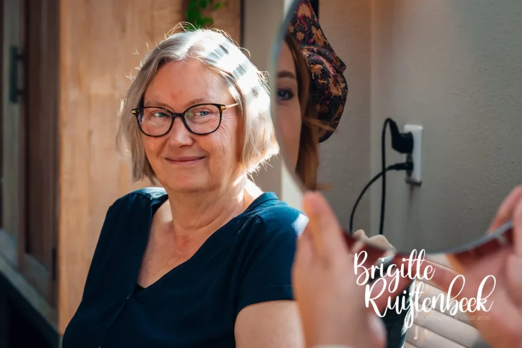 Portret van de moeder van de bruid die glimlacht tijdens het moment van opmaken op de ochtend van de bruiloft bij Trouwboerderij Mausel in Noordbroek.