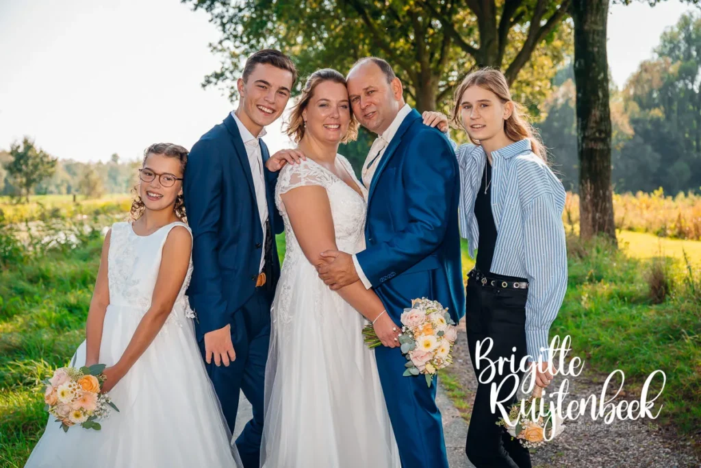Bruidspaar Sandra en David met hun kinderen poserend in een groene omgeving tijdens hun trouwdag bij Trouwboerderij Mausel in Noordbroek.