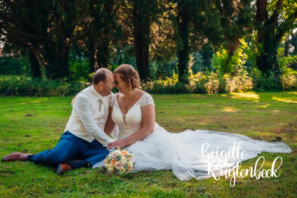 Sandra en David zitten samen in het gras tijdens hun bruiloft bij Trouwboerderij Mausel in Noordbroek