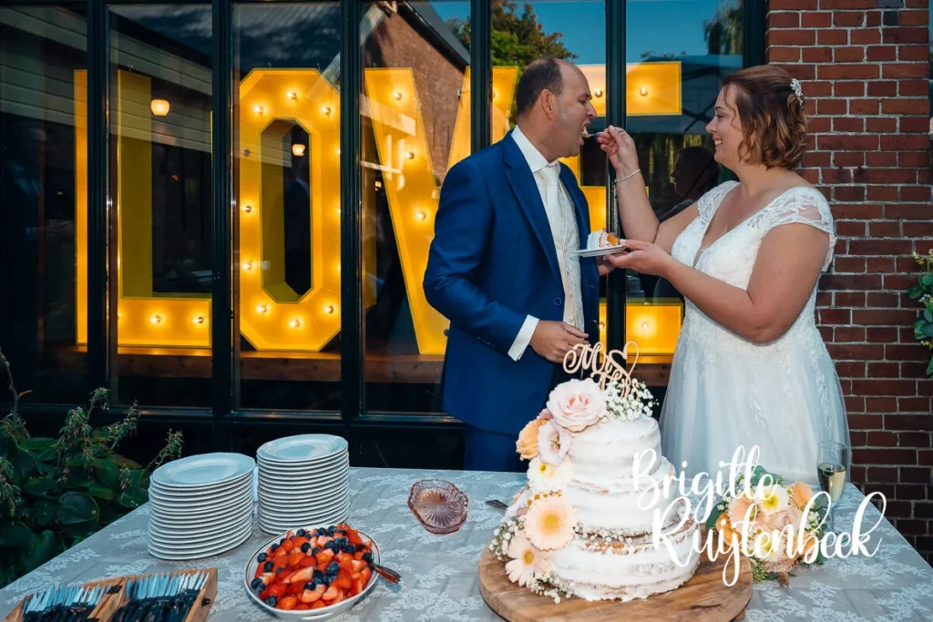Bruid en bruidegom snijden bruidstaart aan buiten bij Trouwboerderij Mausel in Noordbroek.