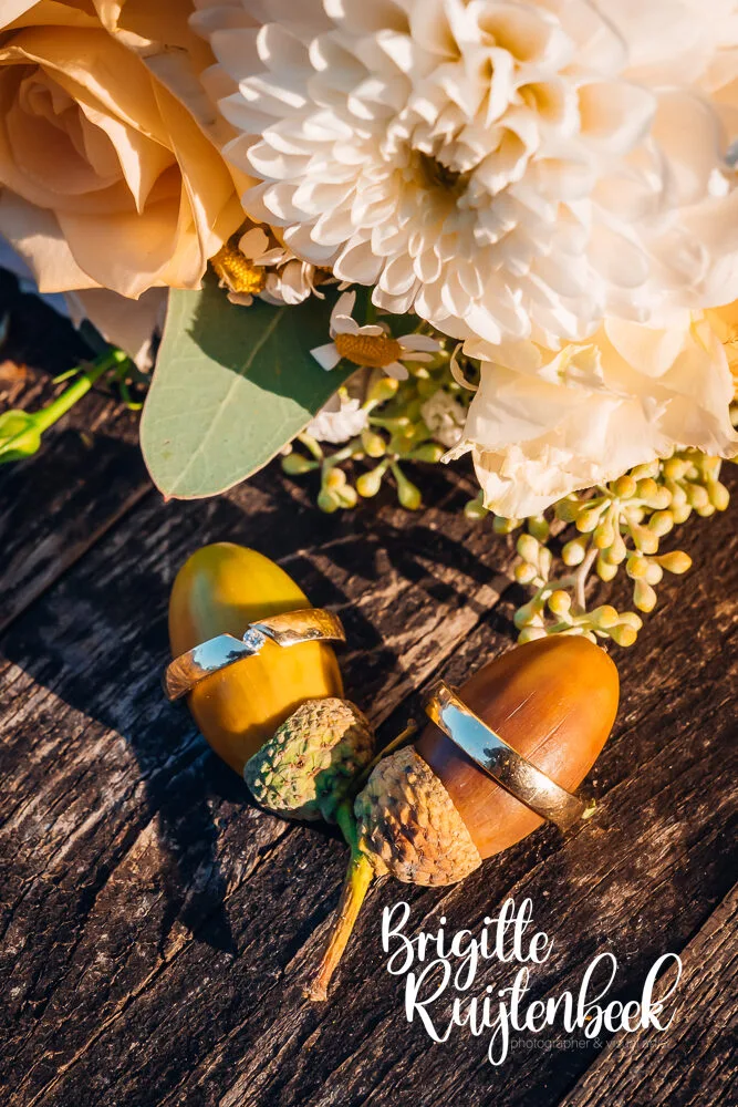 Close-up van trouwringen op eikels met bloemen bij Trouwboerderij Mausel in Noordbroek.