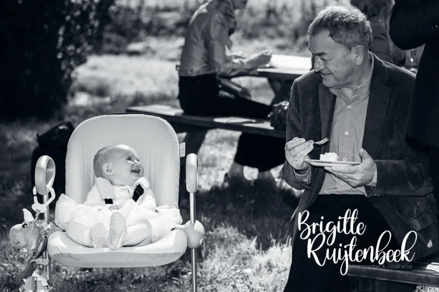 Baby in wipstoel kijkt lachend naar een oudere gast tijdens de bruiloft