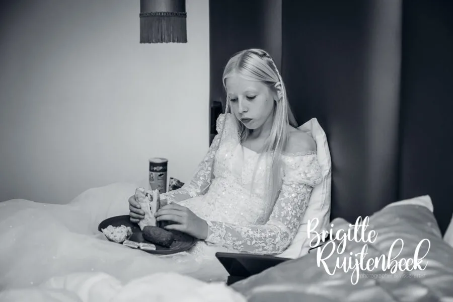 Bruidsmeisje in jurk eet een broodje op bed tijdens een rustig moment op de trouwdag