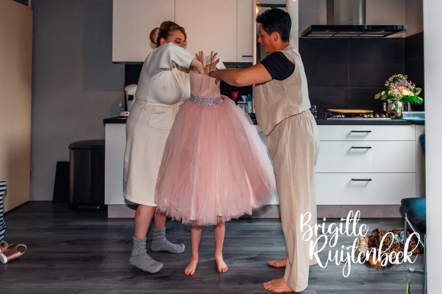 Kind in roze jurk wordt geholpen met aankleden in de keuken tijdens de voorbereidingen