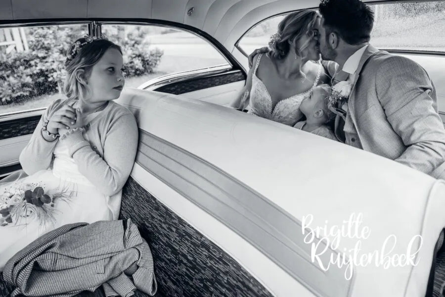 Kind zit apart in de auto terwijl het bruidspaar elkaar kust op de achterbank