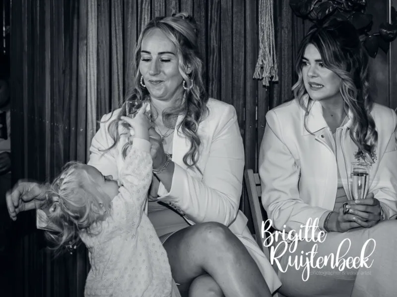 Jong kind reikt omhoog naar een glas terwijl volwassenen naast haar zitten