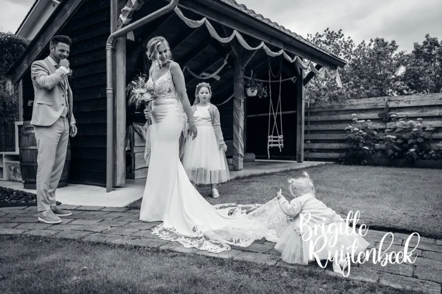 Jong kind speelt met de sleep van de trouwjurk terwijl het bruidspaar toekijkt