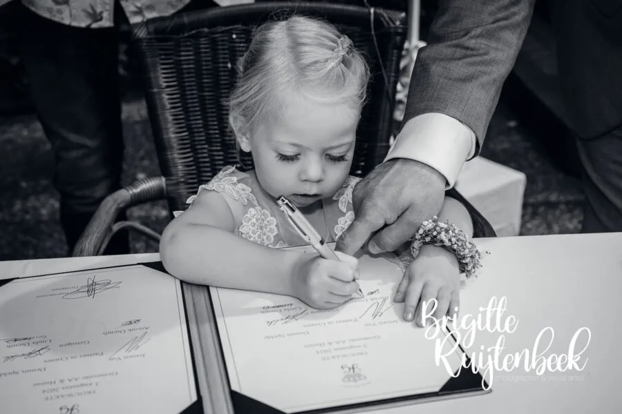 Jong kind tekent mee in het trouwboek terwijl een volwassene helpt