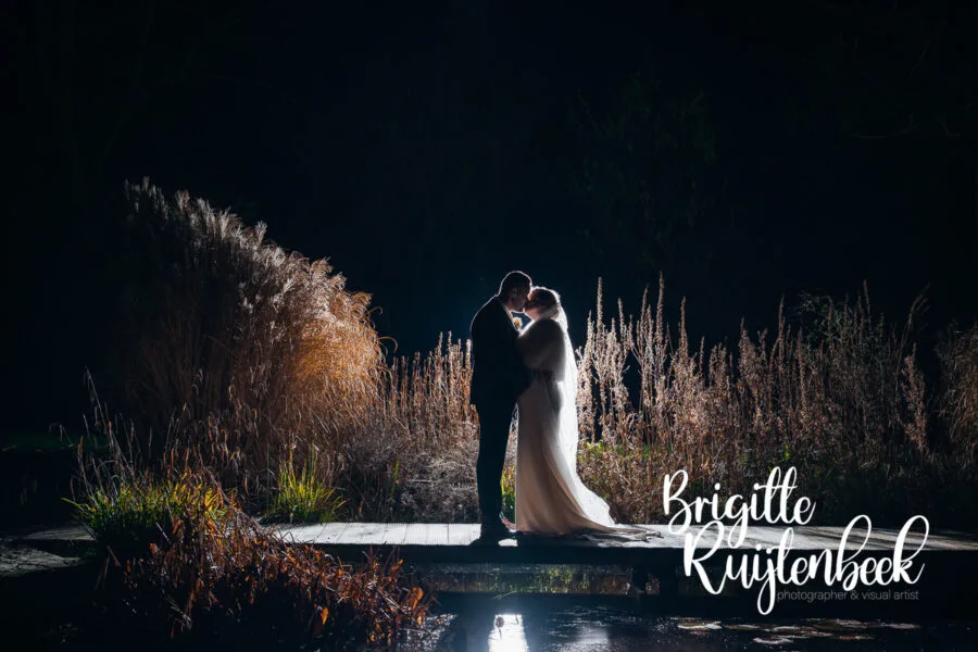 Avondportret van bruid en bruidegom op een bruggetje tijdens een winterbruiloft in Drenthe