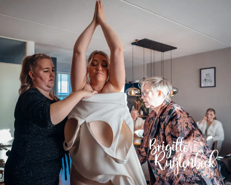 Bruid Tamara wordt geholpen bij het aantrekken van haar trouwjurk tijdens de voorbereidingen van een winterbruiloft in Drenthe