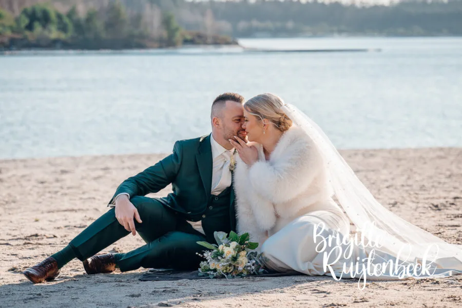 Bruidspaar zit samen aan het water tijdens een winterse fotoshoot bij ’t Nije Hemelriek in Drenthe