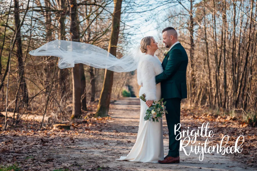 Bruidspaar staat samen op een bospad tijdens een winterse fotoshoot in Drenthe bij ’t Nije Hemelriek