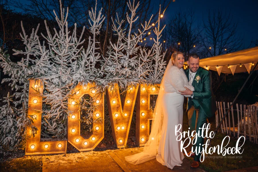 Bruidspaar poseert bij verlichte LOVE-letters tijdens de avond van hun winterbruiloft in Gasselte