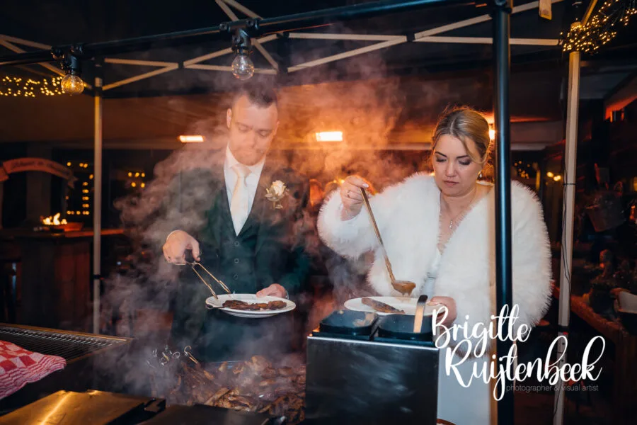 Bruid en bruidegom scheppen samen eten bij de buitenkeuken tijdens hun winterbruiloft in Gasselte