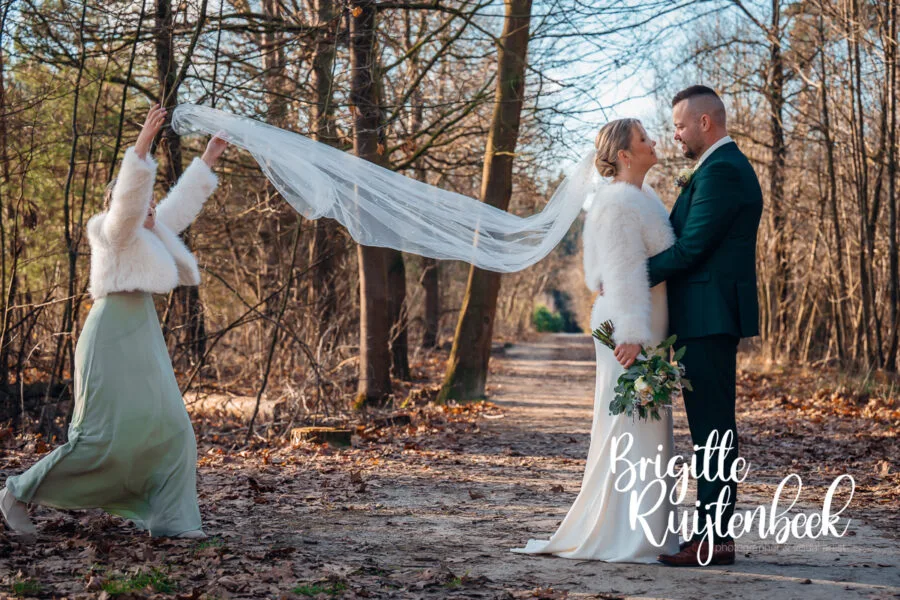 Bruid en bruidegom spelen met de sluier tijdens een winterse fotoshoot in het bos bij Gasselte in Drenthe