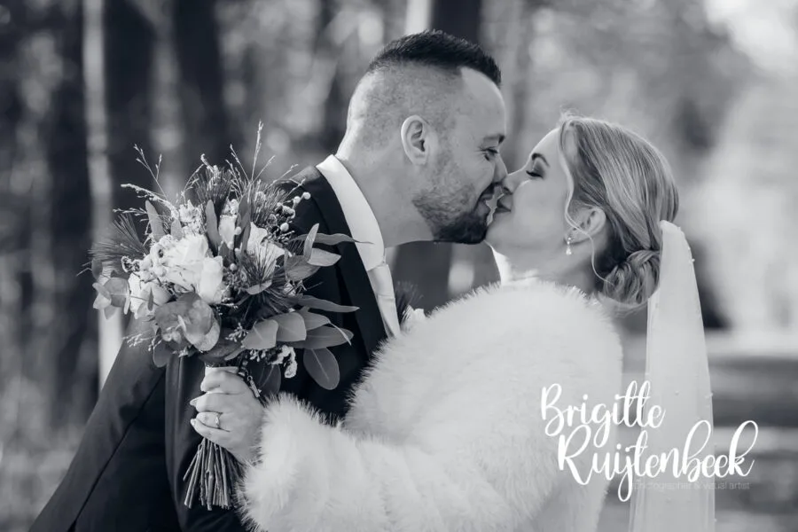 Bruidspaar kust elkaar tijdens een winterse fotoshoot in Drenthe, vastgelegd in zwart-wit bij een winterbruiloft