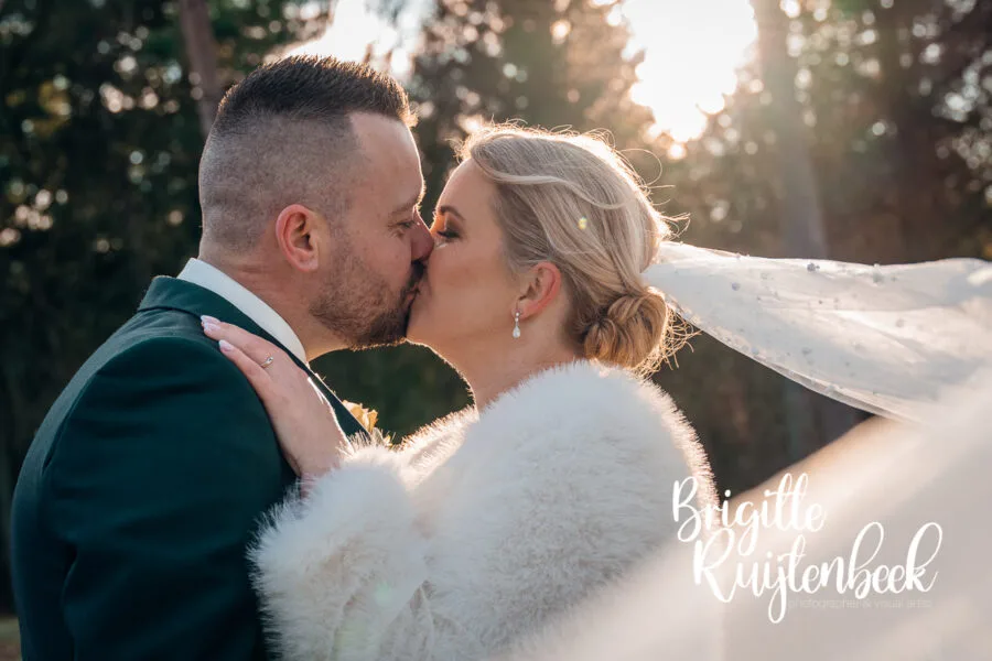 Close-up van een kus tussen bruid en bruidegom met tegenlicht tijdens een winterbruiloft in Drenthe