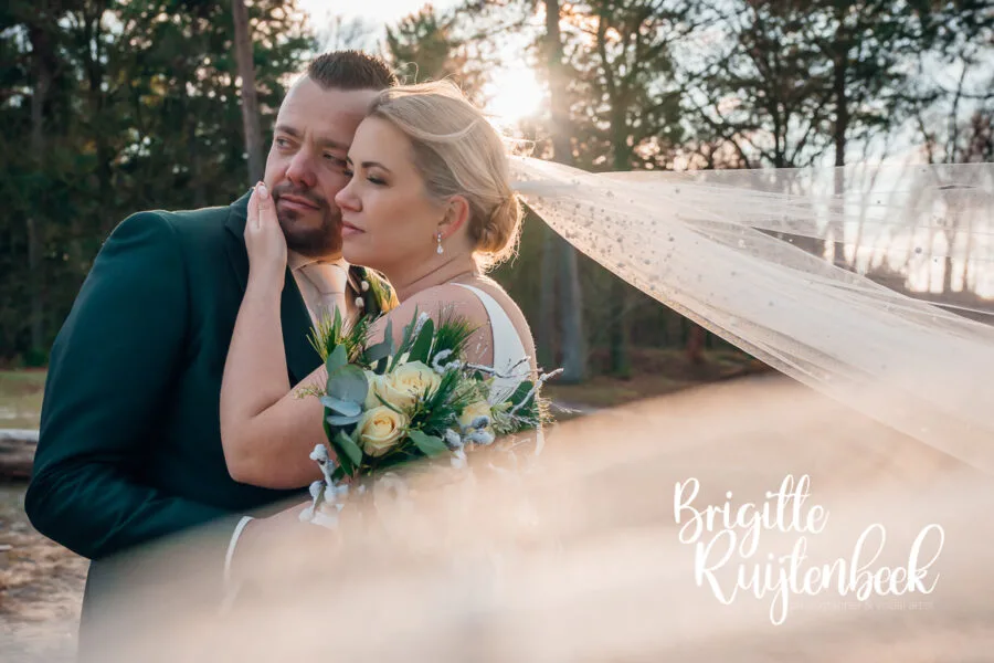 Bruidspaar poseert met sluier en boeket tijdens een winterse fotoshoot in Drenthe