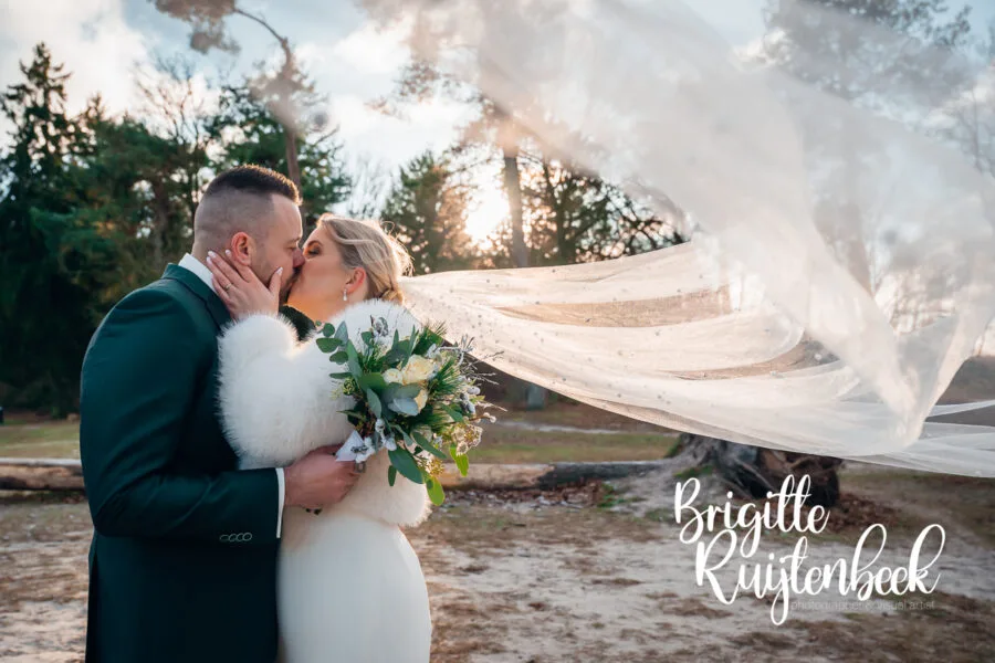 Sluier waait om het bruidspaar heen tijdens een winterse fotoshoot in Drenthe bij ’t Nije Hemelriek