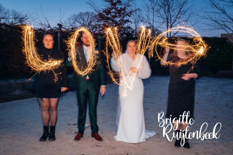 Bruidspaar en vrienden maken een sparklerfoto met het woord love tijdens een winterbruiloft in Drenthe