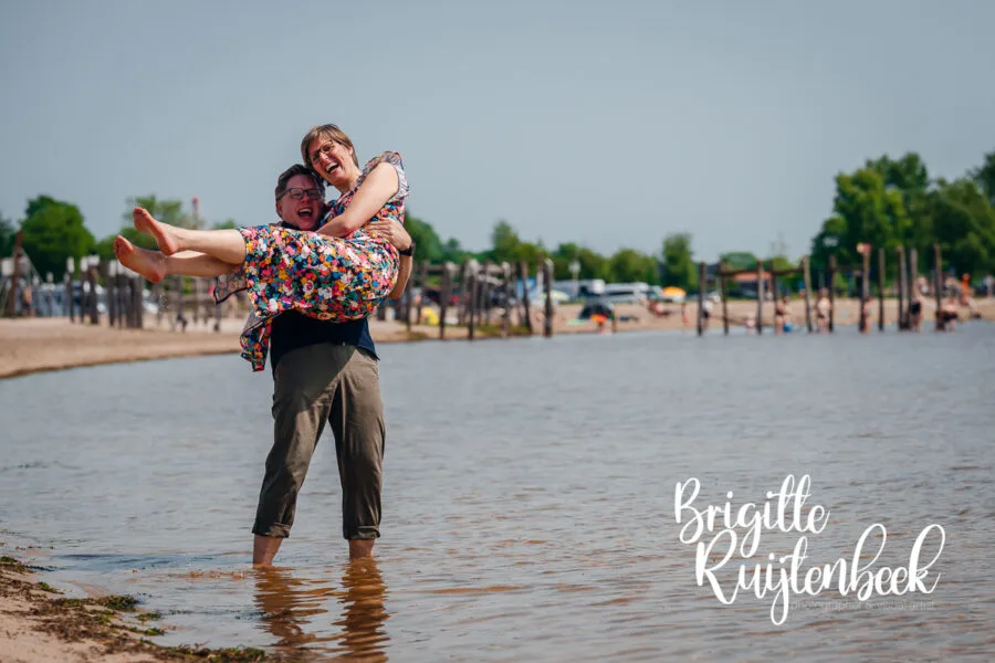 Man tilt zijn vrouw lachend op tijdens een familieshoot aan het Oldambtmeer