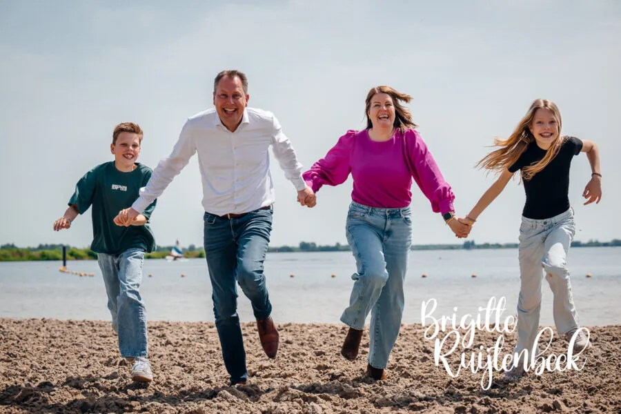 Gezin met twee kinderen rent hand in hand over het strand van het Oldambtmeer tijdens een familieshoot.