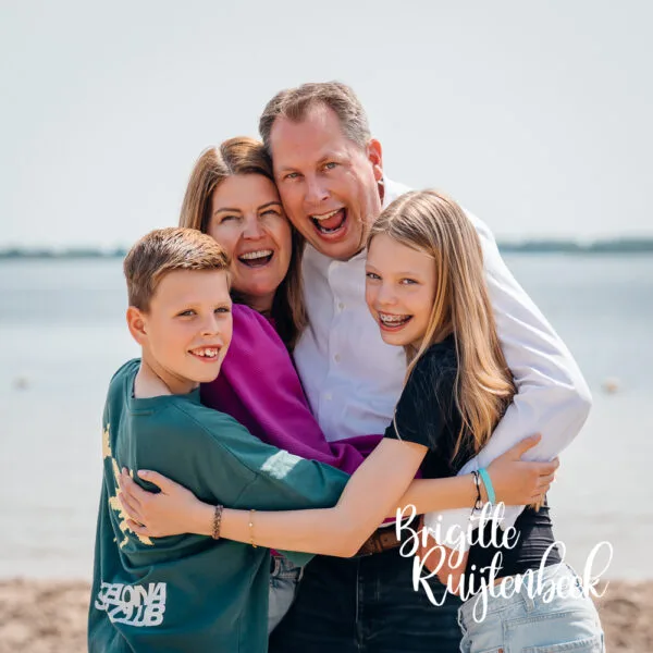 Gezin van vier personen omhelst elkaar tijdens een familieshoot aan het Oldambtmeer.