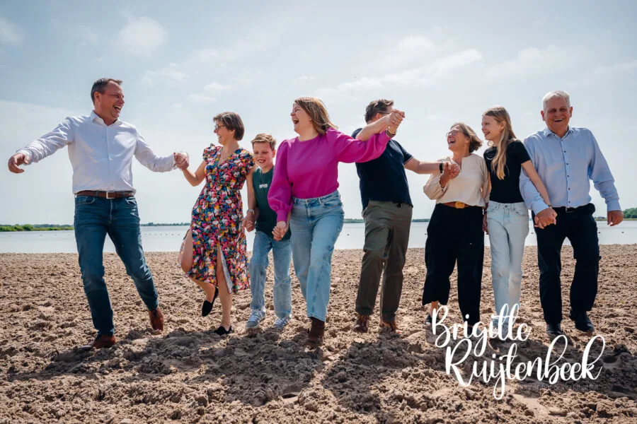 Familie wandelt lachend hand in hand over het strand tijdens een familieshoot aan het Oldambtmeer.