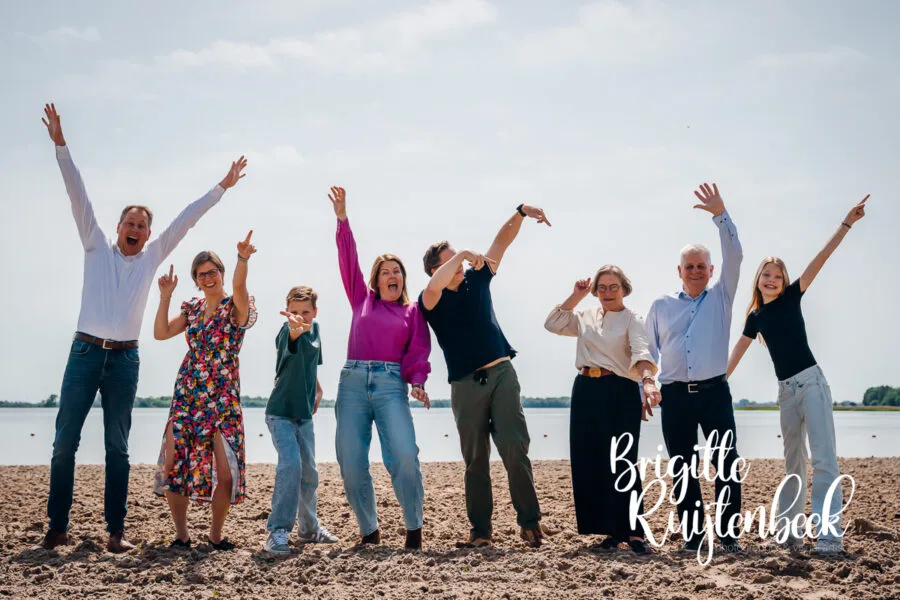 Familie poseert vrolijk met opgeheven armen tijdens een familieshoot op het strand van het Oldambtmeer.