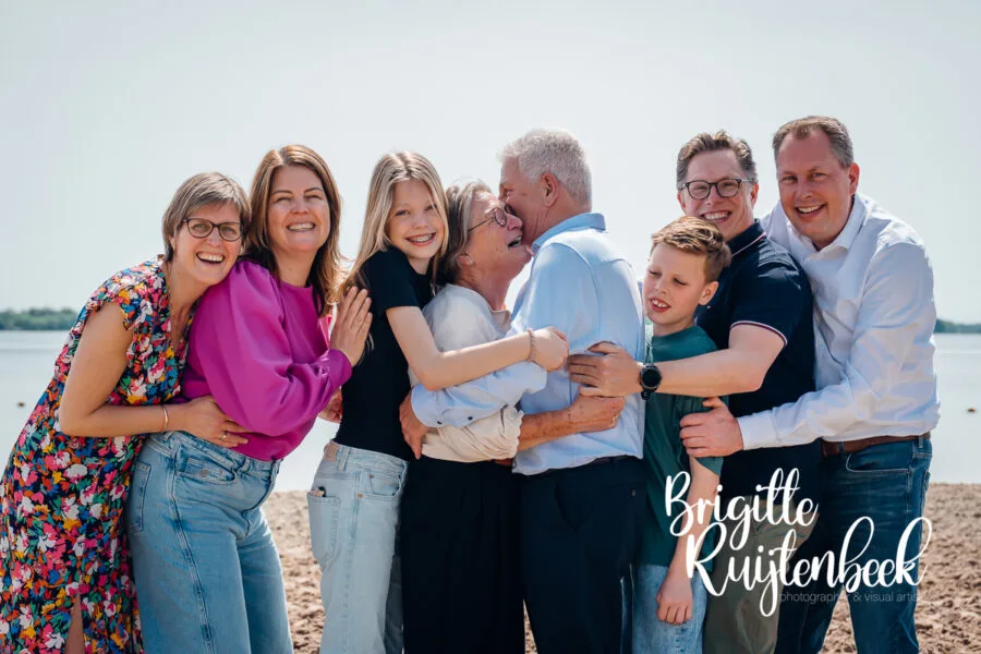 Opa, oma, kinderen en kleinkinderen omhelzen elkaar tijdens een familieshoot aan het Oldambtmeer.